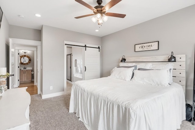 bedroom with ceiling fan, ensuite bathroom, a barn door, and light carpet