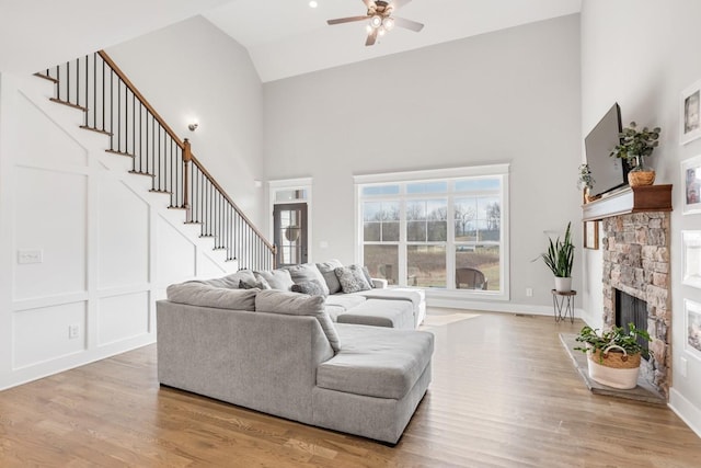 living room featuring high vaulted ceiling, a stone fireplace, light hardwood / wood-style floors, and ceiling fan