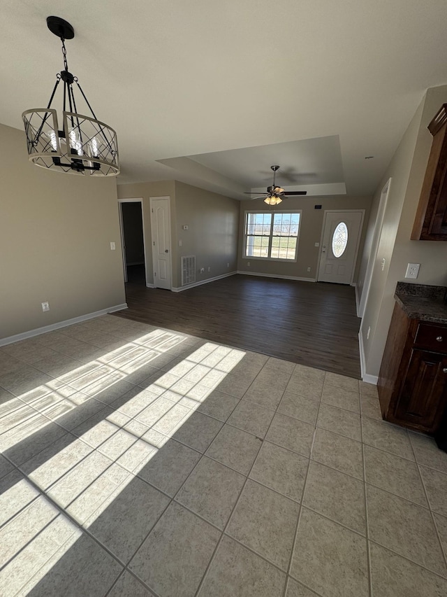 unfurnished living room featuring tile patterned flooring, a tray ceiling, and ceiling fan with notable chandelier