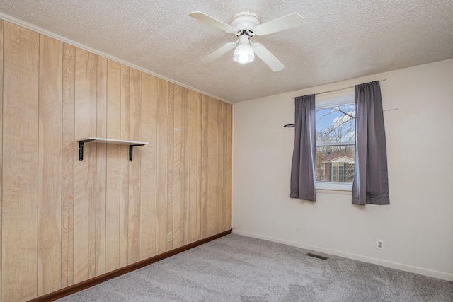 carpeted empty room featuring ceiling fan, a textured ceiling, and wood walls