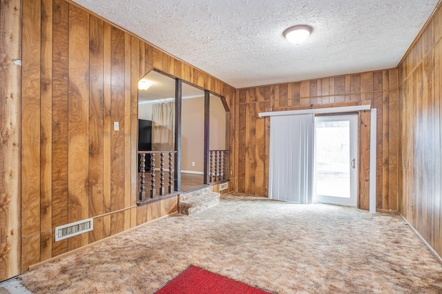 empty room with wooden walls, carpet floors, and a textured ceiling