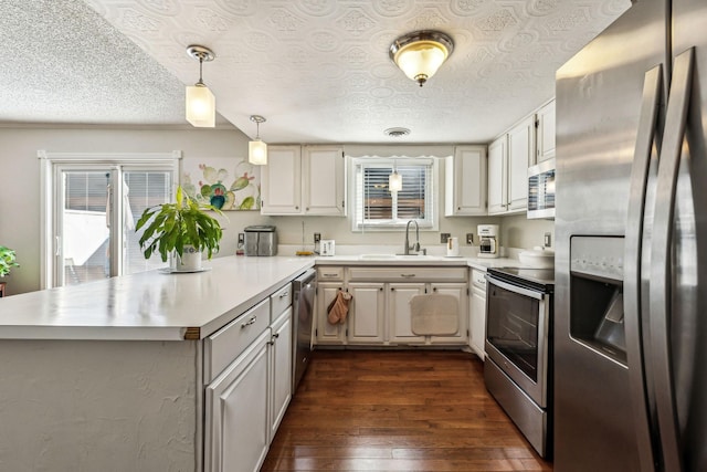 kitchen featuring sink, appliances with stainless steel finishes, white cabinetry, hanging light fixtures, and kitchen peninsula