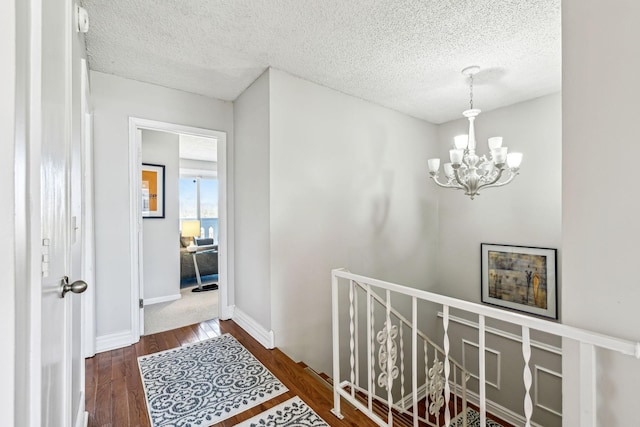 corridor with a textured ceiling, a notable chandelier, and dark hardwood / wood-style flooring