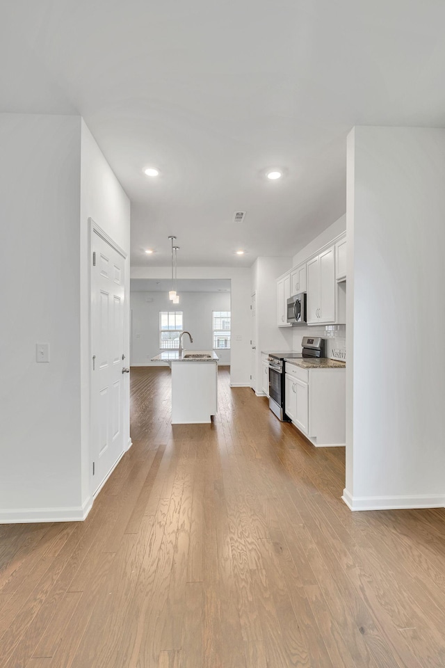 kitchen with white cabinetry, decorative light fixtures, a center island with sink, light hardwood / wood-style flooring, and appliances with stainless steel finishes