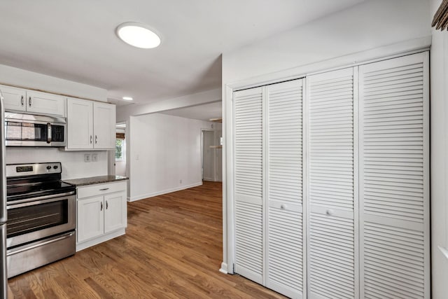 kitchen featuring hardwood / wood-style flooring, stainless steel appliances, dark stone counters, and white cabinets