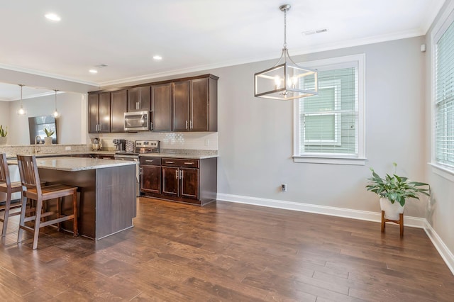 kitchen with appliances with stainless steel finishes, a breakfast bar, pendant lighting, dark brown cabinetry, and light stone countertops