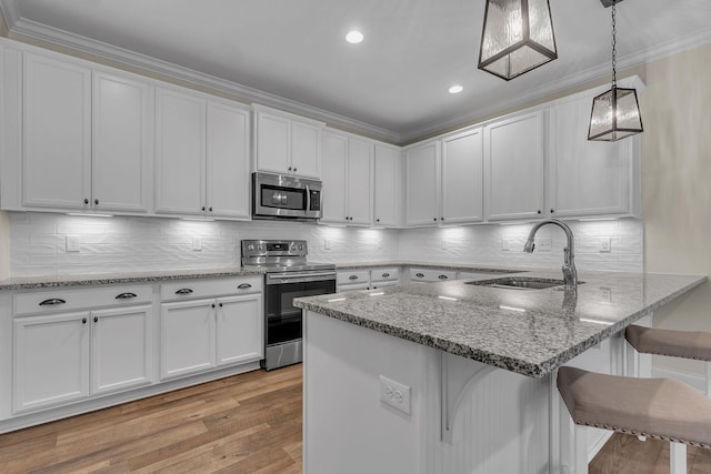 kitchen with pendant lighting, appliances with stainless steel finishes, a kitchen breakfast bar, and white cabinets