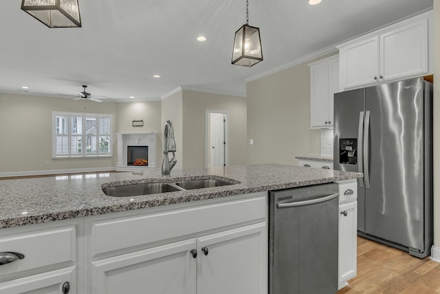 kitchen with appliances with stainless steel finishes, white cabinetry, sink, hanging light fixtures, and light stone countertops