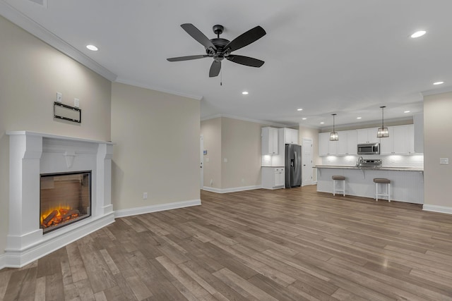 unfurnished living room with ornamental molding, ceiling fan, and light wood-type flooring