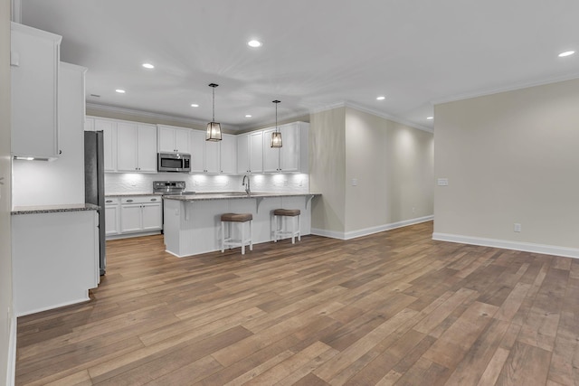 kitchen featuring hanging light fixtures, appliances with stainless steel finishes, white cabinets, light hardwood / wood-style floors, and backsplash