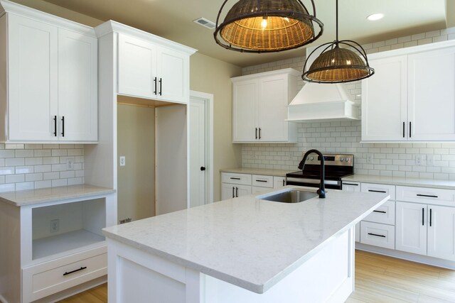 kitchen featuring white cabinets, light stone counters, premium range hood, and a sink