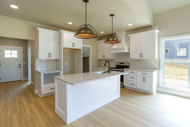 kitchen with stainless steel electric range oven, light wood finished floors, a kitchen island with sink, a sink, and white cabinetry