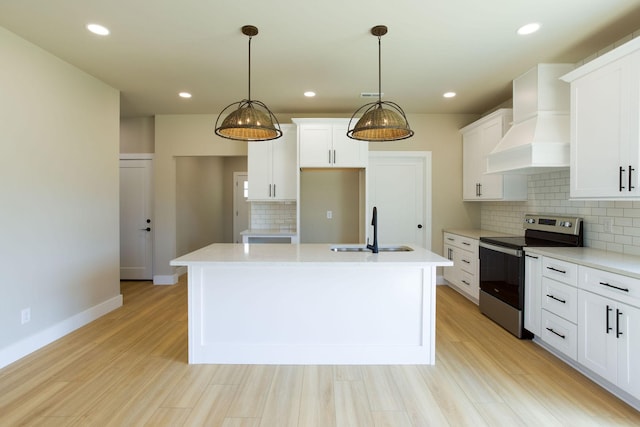 kitchen with stainless steel electric stove, a center island with sink, light countertops, custom range hood, and a sink