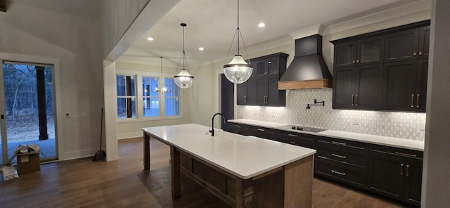 kitchen featuring premium range hood, a breakfast bar area, hanging light fixtures, a center island with sink, and black electric cooktop