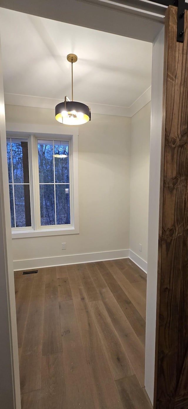 spare room with dark wood-type flooring, ornamental molding, and a barn door