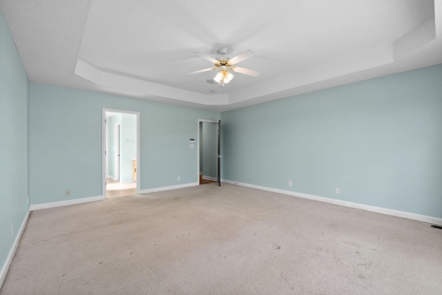 empty room with a tray ceiling, a ceiling fan, light colored carpet, and baseboards