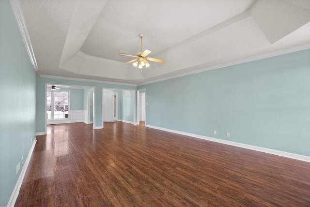 unfurnished room featuring baseboards, dark wood-style floors, ceiling fan, ornamental molding, and a tray ceiling