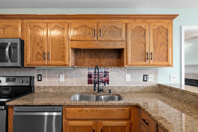 kitchen with light stone counters, a sink, appliances with stainless steel finishes, backsplash, and brown cabinets