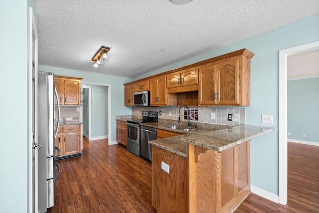 kitchen featuring brown cabinets, appliances with stainless steel finishes, dark wood-type flooring, a sink, and a peninsula