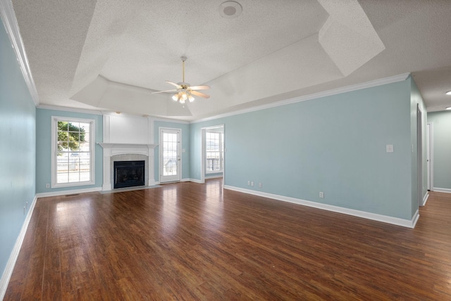 unfurnished living room featuring a fireplace, a raised ceiling, dark wood finished floors, and a healthy amount of sunlight