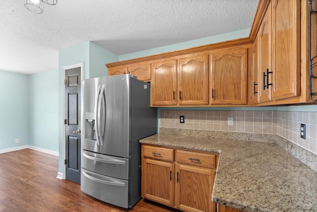 kitchen featuring light stone counters, dark wood-style flooring, stainless steel refrigerator with ice dispenser, and decorative backsplash