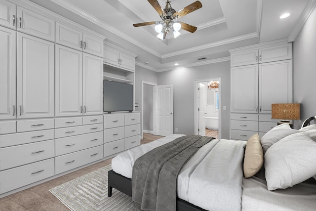 carpeted bedroom featuring a tray ceiling, ensuite bath, ornamental molding, and ceiling fan