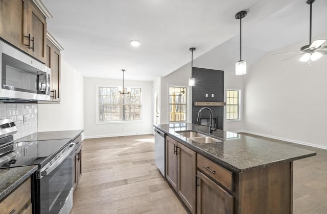 kitchen featuring appliances with stainless steel finishes, pendant lighting, a large fireplace, sink, and a center island with sink