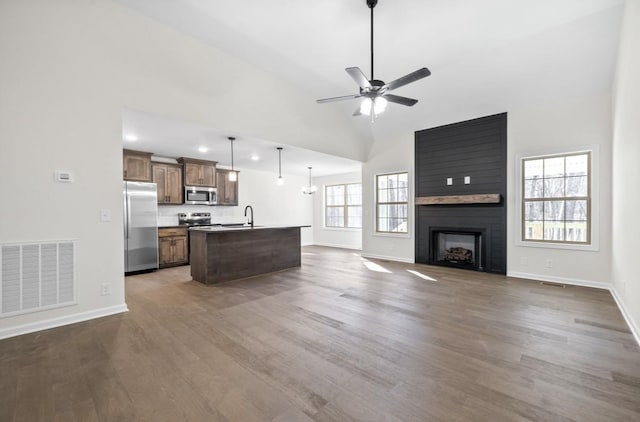 kitchen with sink, hanging light fixtures, stainless steel appliances, a fireplace, and a kitchen island with sink