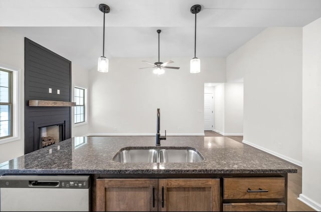 kitchen featuring sink, dishwasher, dark stone countertops, hanging light fixtures, and a fireplace