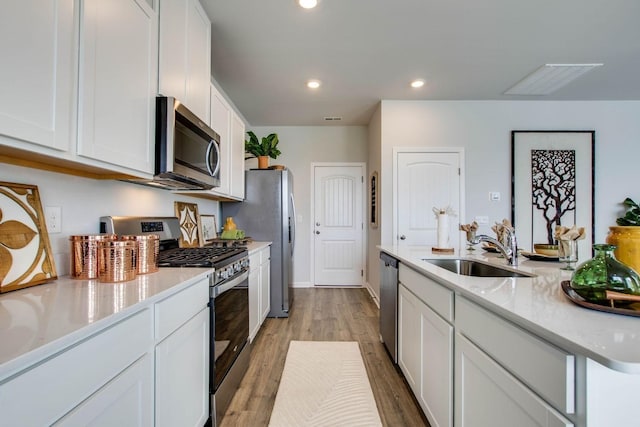 kitchen featuring stainless steel appliances, white cabinetry, sink, and light wood-type flooring