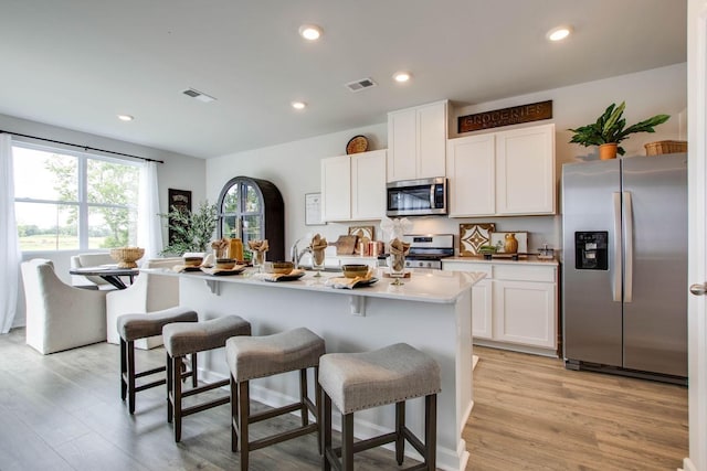 kitchen with an island with sink, appliances with stainless steel finishes, white cabinets, and a kitchen breakfast bar