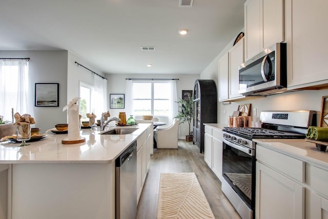 kitchen with sink, light hardwood / wood-style flooring, stainless steel appliances, a kitchen island with sink, and white cabinets