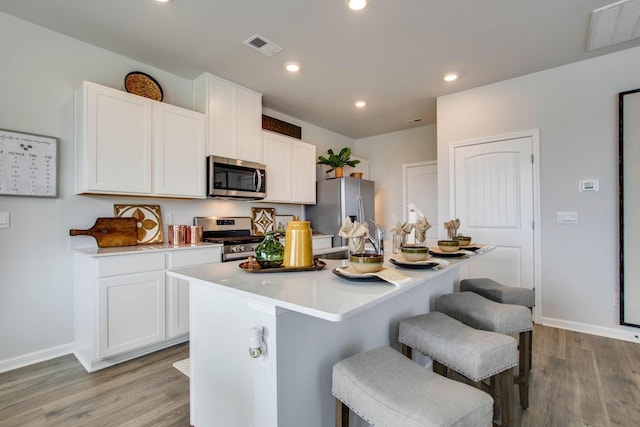 kitchen with a kitchen island with sink, stainless steel appliances, and white cabinets