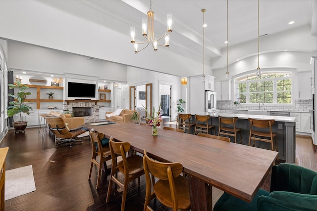 dining space featuring dark wood-type flooring, a towering ceiling, a fireplace, and an inviting chandelier