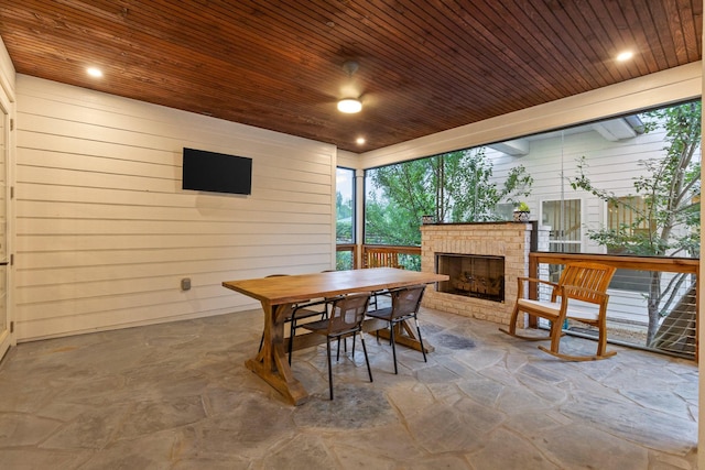 dining area featuring an outdoor brick fireplace, wooden walls, and wooden ceiling