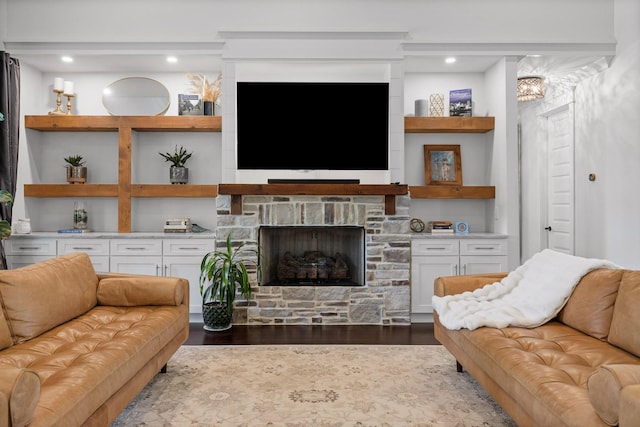 living room featuring built in shelves, dark hardwood / wood-style floors, and a stone fireplace