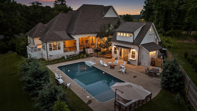 back house at dusk featuring an outdoor structure, a fenced in pool, and a patio