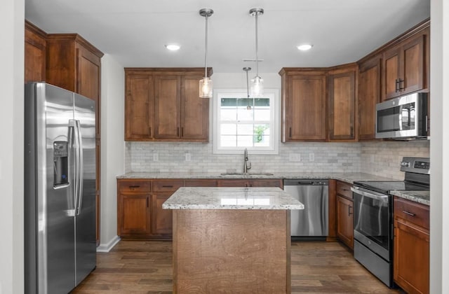 kitchen with sink, appliances with stainless steel finishes, a center island, light stone counters, and decorative light fixtures