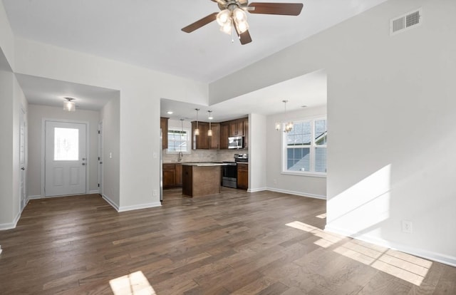 unfurnished living room with dark hardwood / wood-style flooring, ceiling fan with notable chandelier, and a healthy amount of sunlight