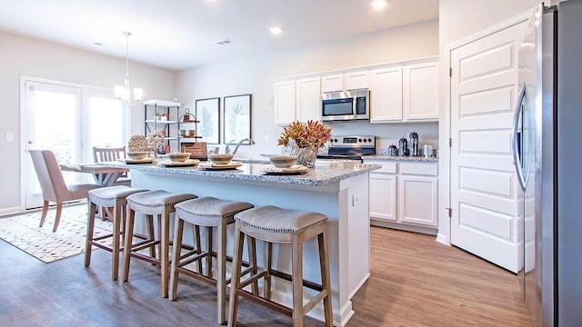 kitchen with pendant lighting, an island with sink, white cabinets, stainless steel appliances, and light stone countertops