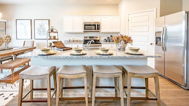 kitchen with white cabinetry, appliances with stainless steel finishes, a kitchen island with sink, and light stone counters