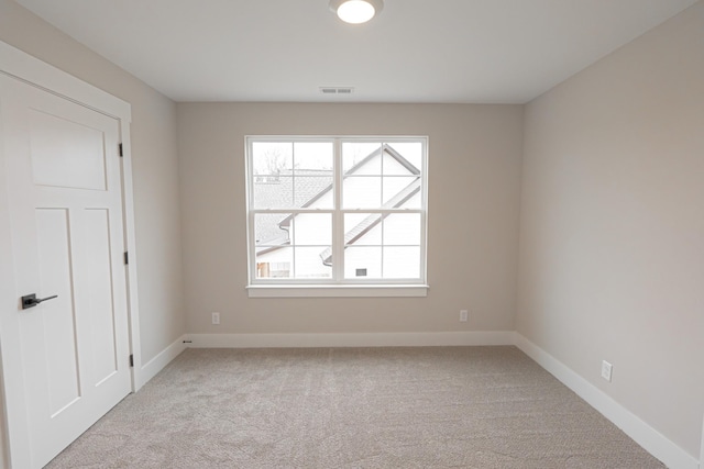 spare room with light colored carpet, a healthy amount of sunlight, visible vents, and baseboards