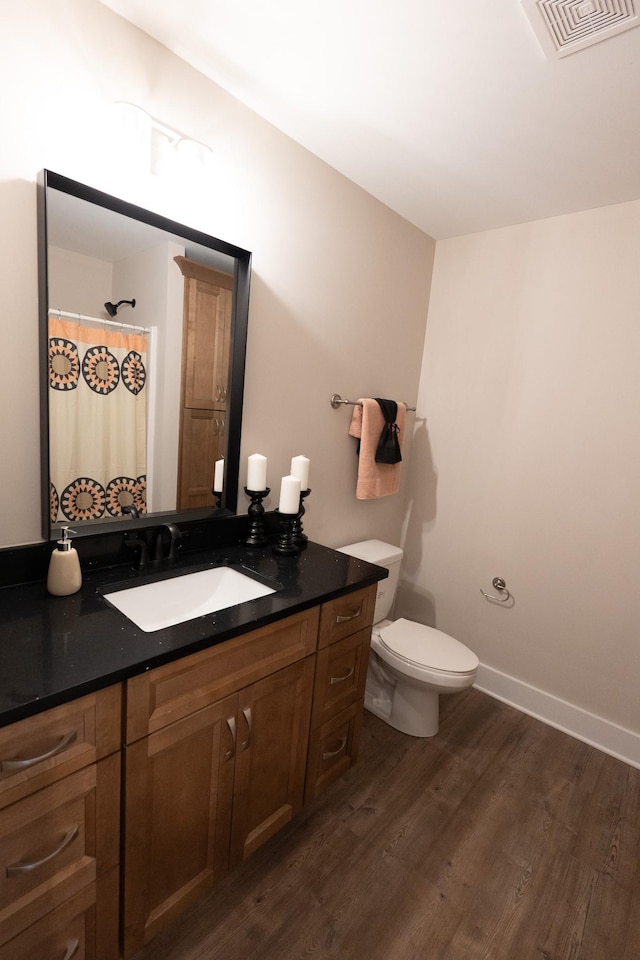 bathroom featuring baseboards, visible vents, toilet, wood finished floors, and vanity