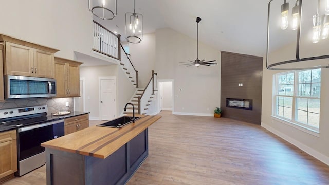 kitchen with a kitchen island, appliances with stainless steel finishes, a large fireplace, sink, and wooden counters