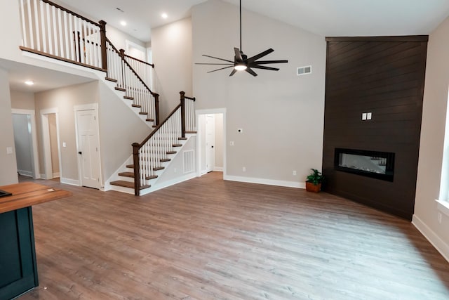 unfurnished living room with hardwood / wood-style flooring, a large fireplace, ceiling fan, and a towering ceiling