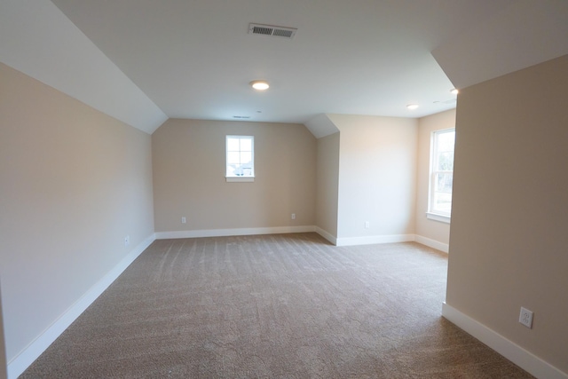 additional living space with visible vents, vaulted ceiling, light carpet, and baseboards