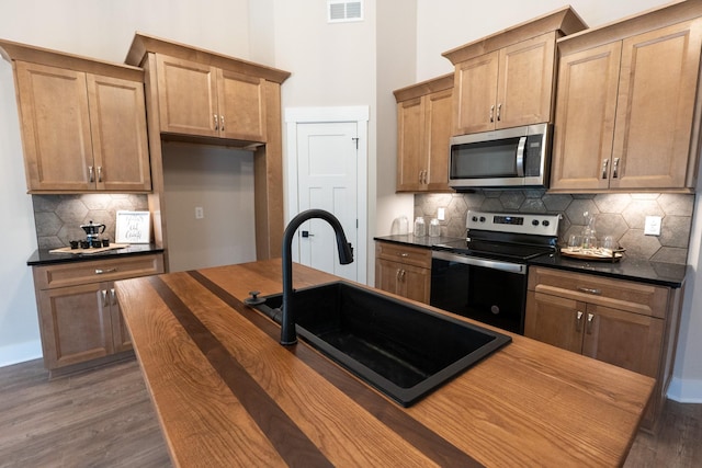 kitchen featuring stainless steel appliances, dark countertops, visible vents, brown cabinetry, and a sink