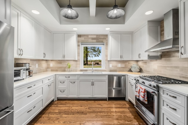 kitchen with pendant lighting, sink, stainless steel appliances, white cabinets, and wall chimney exhaust hood