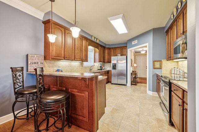 kitchen featuring pendant lighting, appliances with stainless steel finishes, a kitchen bar, and backsplash