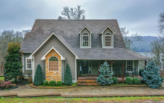 view of front of house with stone siding, covered porch, and roof with shingles